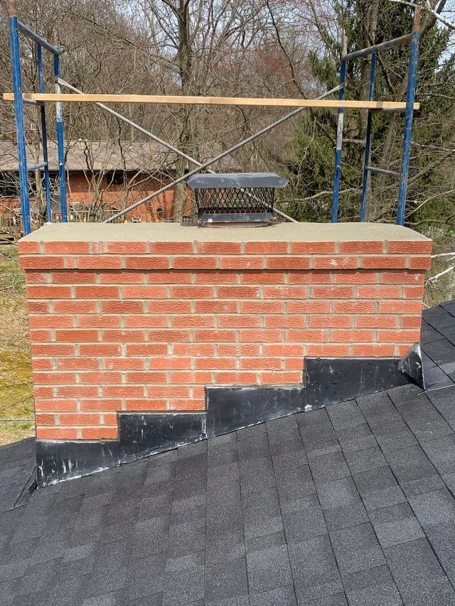 Brick chimney with a metal cap and scaffolding, on a roof.