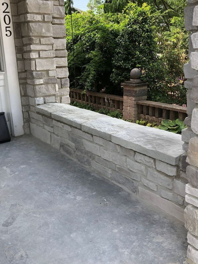 Gray stone porch with a low wall, leading to a green-treed garden.
