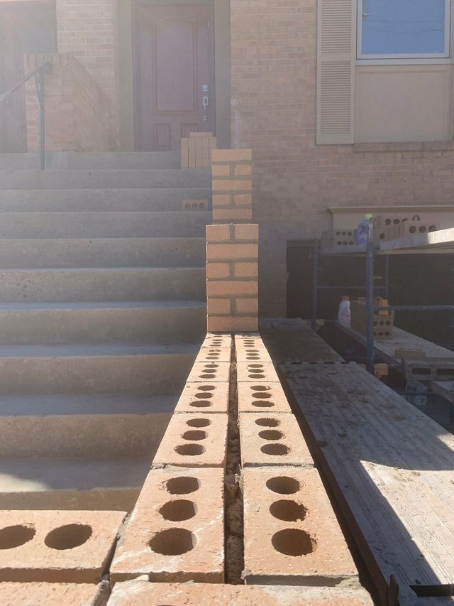 Brickwork in progress at house entrance; steps, partially built wall, and scaffolding visible.