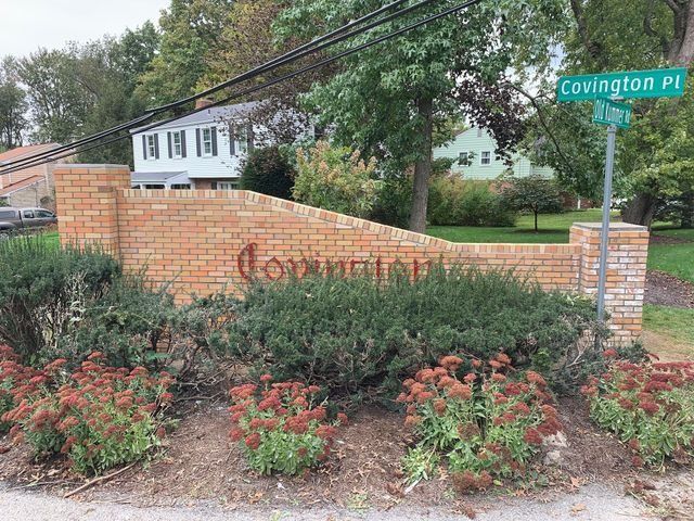 Brick sign at Covington Place entrance with green street sign, shrubs, and houses.