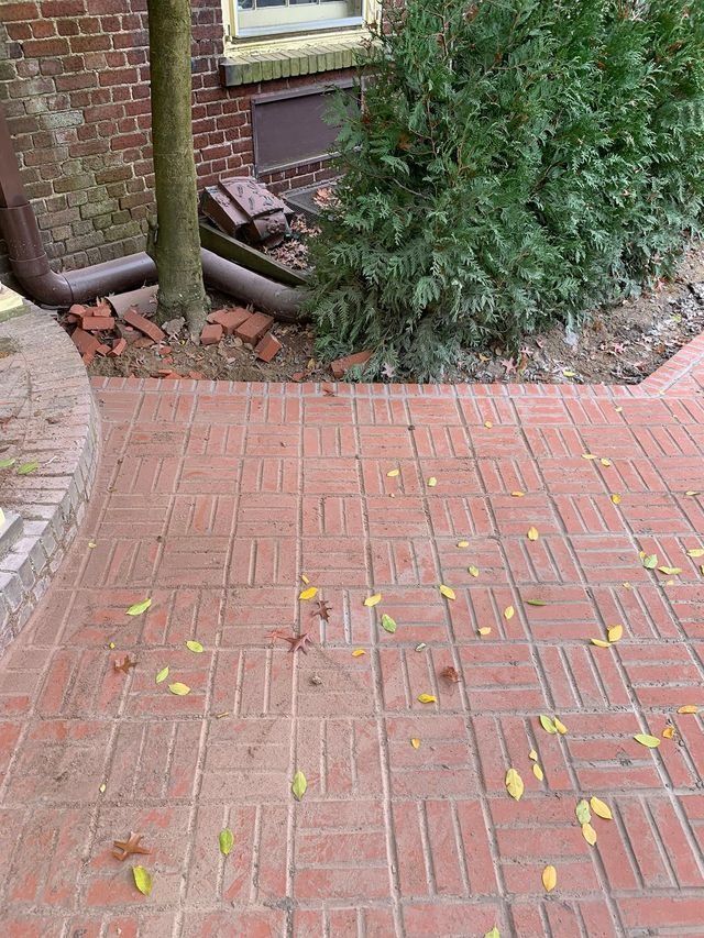 Red brick pathway leading to a brick building with a tree and green bush on the side.