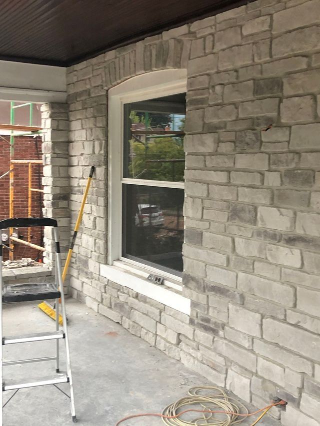 Stone facade with a window and porch under construction; scaffolding visible.