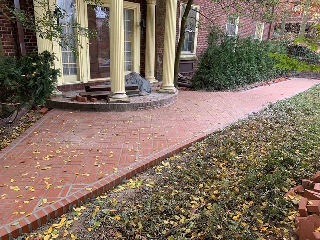 Red brick pathway leading to a house with columns, leaves scattered about.