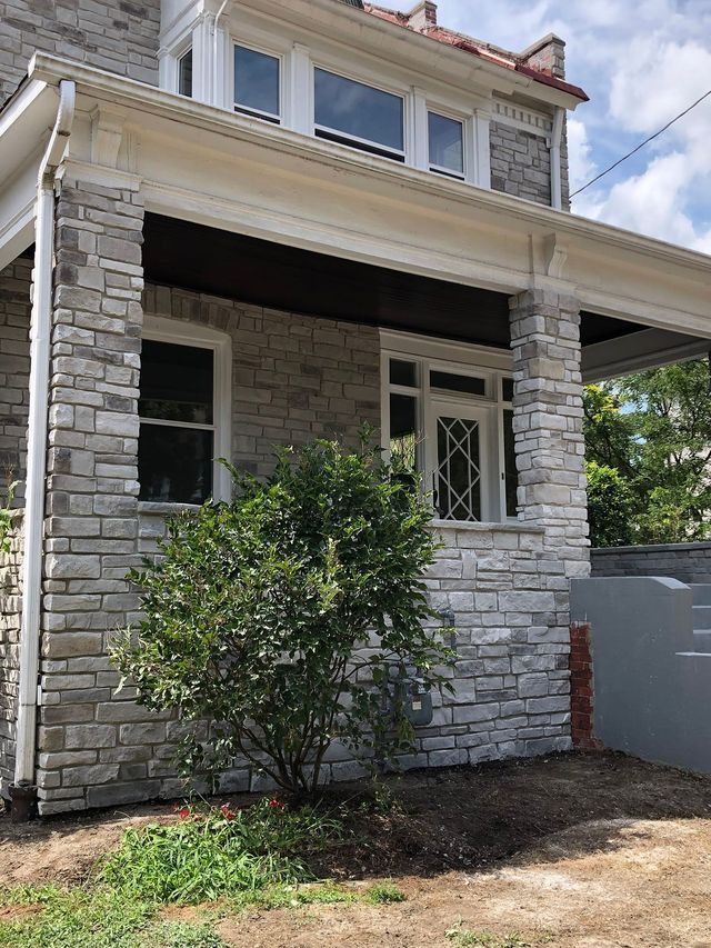 Stone house exterior with porch, windows, and a small green bush.