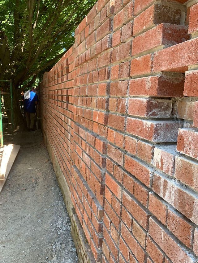 Brick wall with missing sections, along a pathway, person in background.