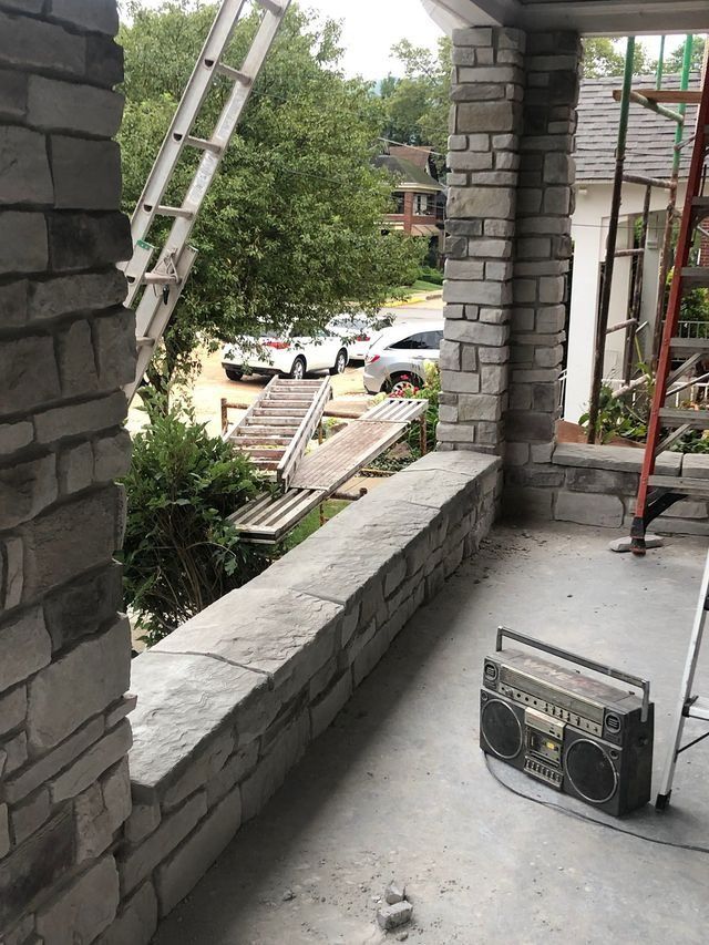 Construction site: stone porch with a boombox, ladders, and a ramp; cars and trees in the background.