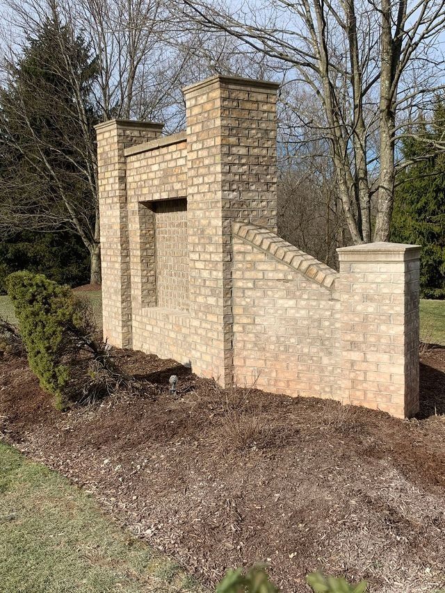 Brick wall with stepped design in a garden setting, with bare mulch.