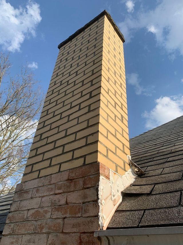 Tall brick chimney rising from a dark shingled roof against a blue sky.