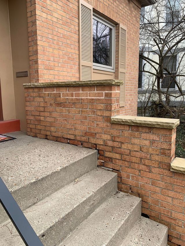 Brick steps leading up to a house with brick walls and a window with shutters.