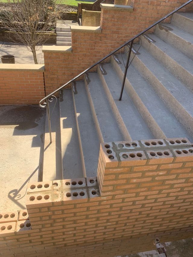 Brick stairs with metal handrail under construction outdoors.