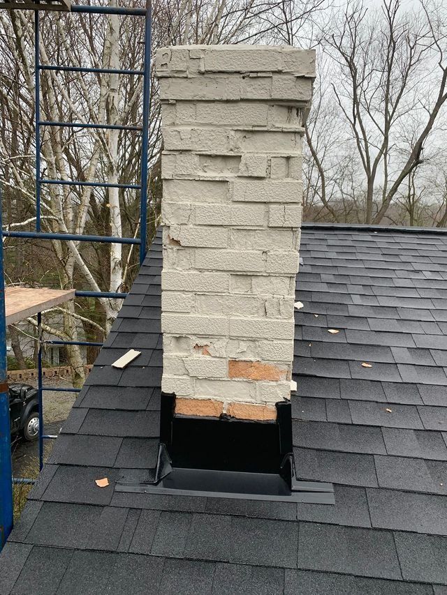 Chimney with crumbling bricks on a rooftop, next to scaffolding and trees.