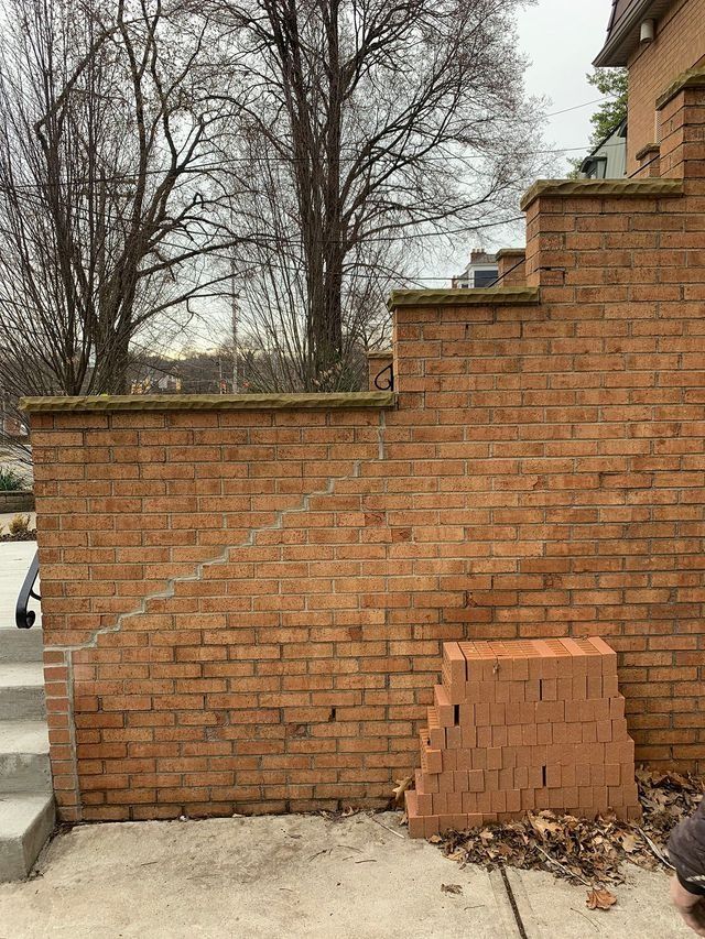 Brick retaining wall with stairs, stack of bricks, trees.