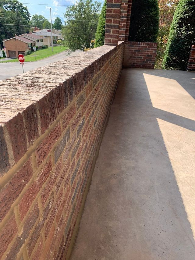 Brick wall extending along a concrete surface, adjacent to a street.