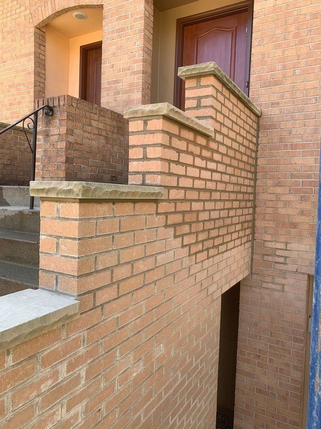 Brick steps leading to a doorway with a brick wall and a handrail on the left side.