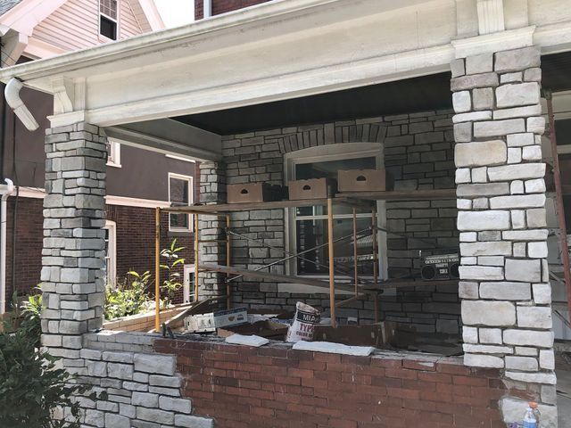 Stone facade being applied to a brick porch of a house under construction with scaffolding.