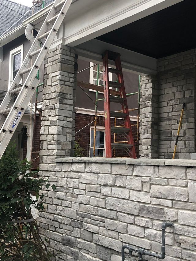 Exterior house with stone veneer being installed. Ladders, scaffolding, and construction in progress.