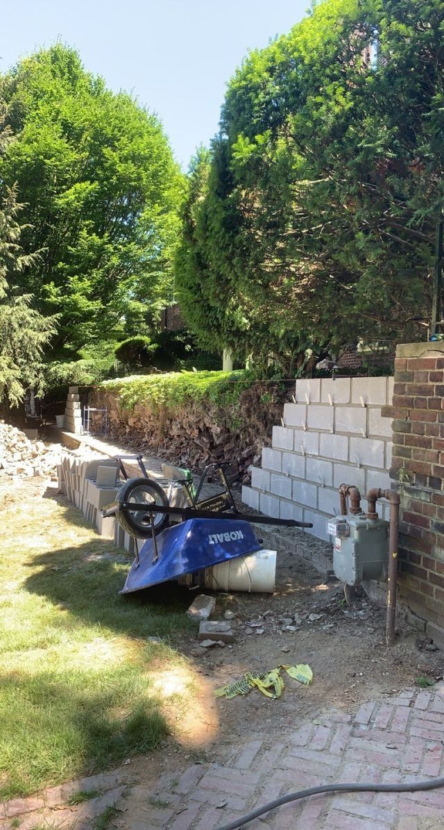 Blue wheelbarrow near a retaining wall made of cinder blocks, trees in the background, sunny day.