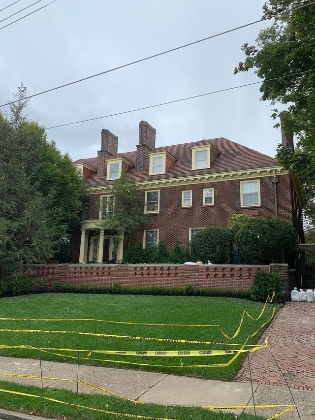 Brick mansion with a brick wall, green lawn, and caution tape on a cloudy day.