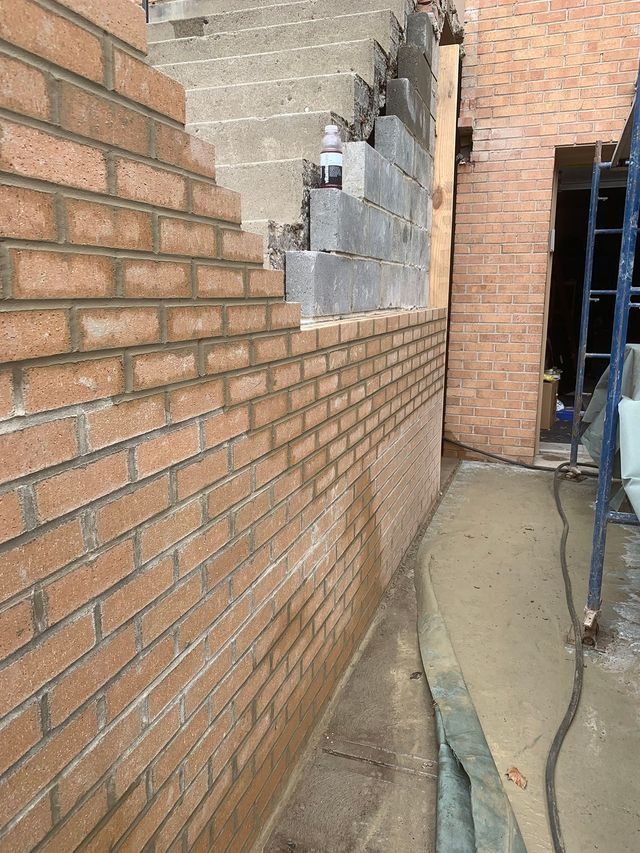 Brick wall being built next to a concrete staircase. Construction site setting.