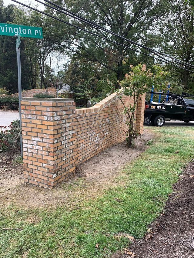Brick wall along a road with a street sign, Covington Pl, and a small tree. A black truck is parked nearby.