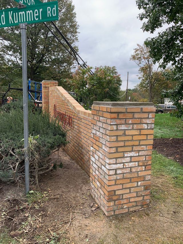 Brick wall with entrance sign, near a road sign that reads 