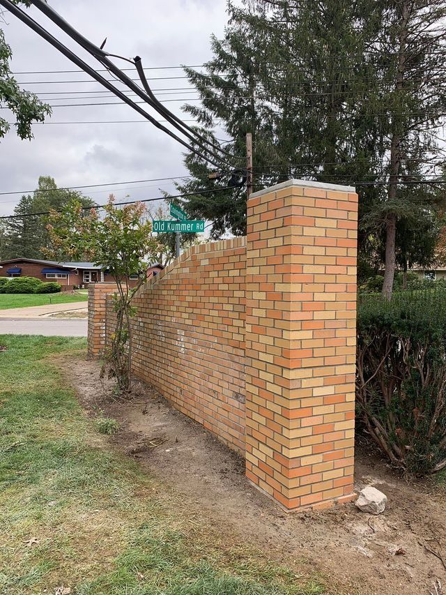 Brick wall with a street sign, surrounded by grass and trees.