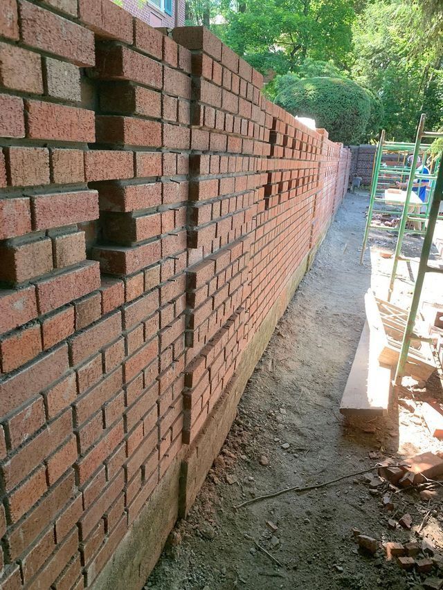 Brick wall under construction, red bricks, mortar, unfinished sections. Outdoor setting.