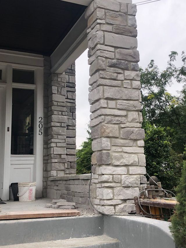 Stone column supporting a porch roof at house 205, under construction with exposed concrete and steps.