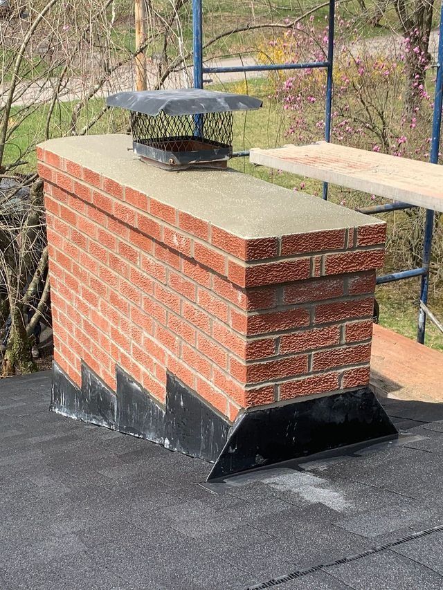 Brick chimney with angled black flashing on a black roof.