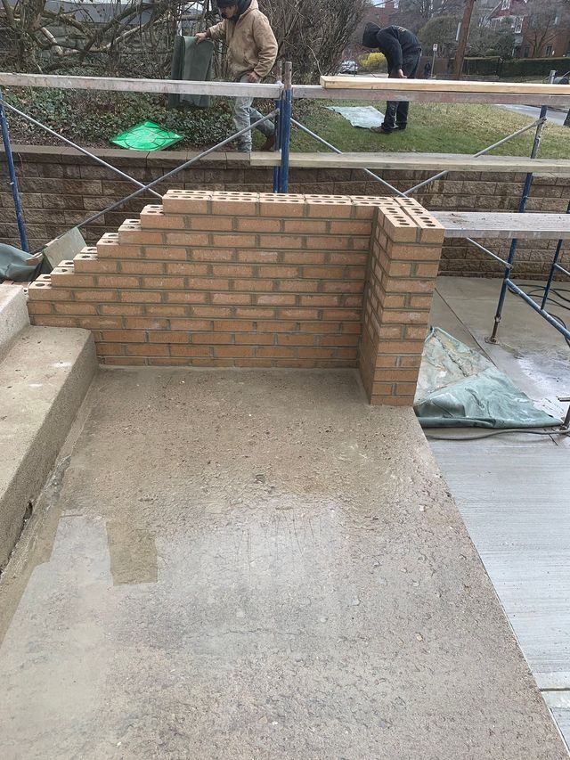 Brick wall being built on concrete steps; workers in background.