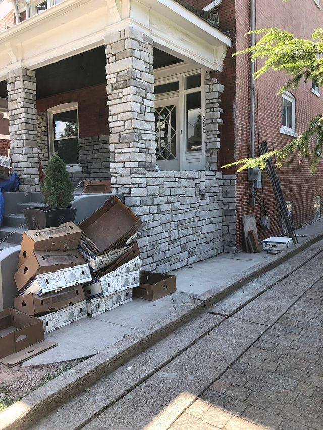 A stone-faced porch being worked on, with cardboard boxes stacked in front of it on a sidewalk next to a brick street.