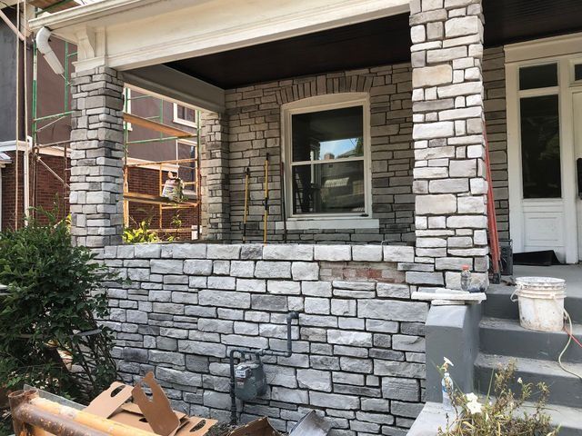 Stone veneer facade of a porch being installed. Gray stones, window, and columns. Construction in progress.