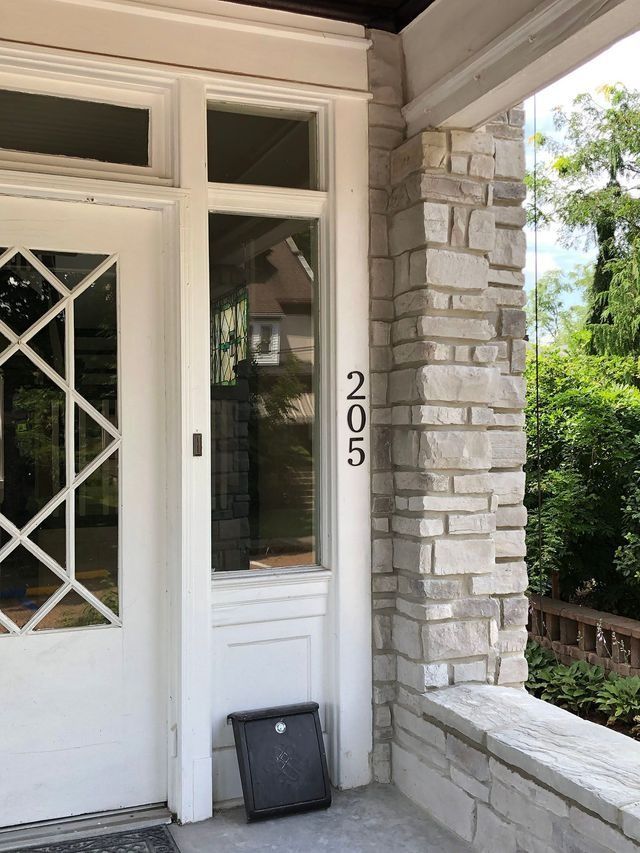 White front door with sidelight and house number 205 on a stone pillar.