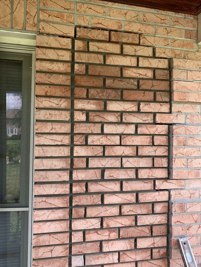 Brick wall with a section removed, revealing a darker brick pattern, next to a window.
