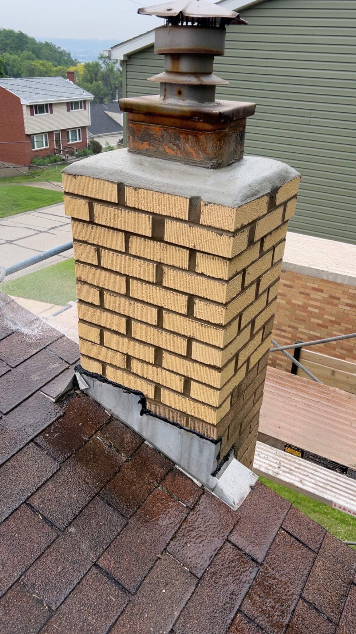 Brick chimney on a shingled roof, with a metal cap and flashing.