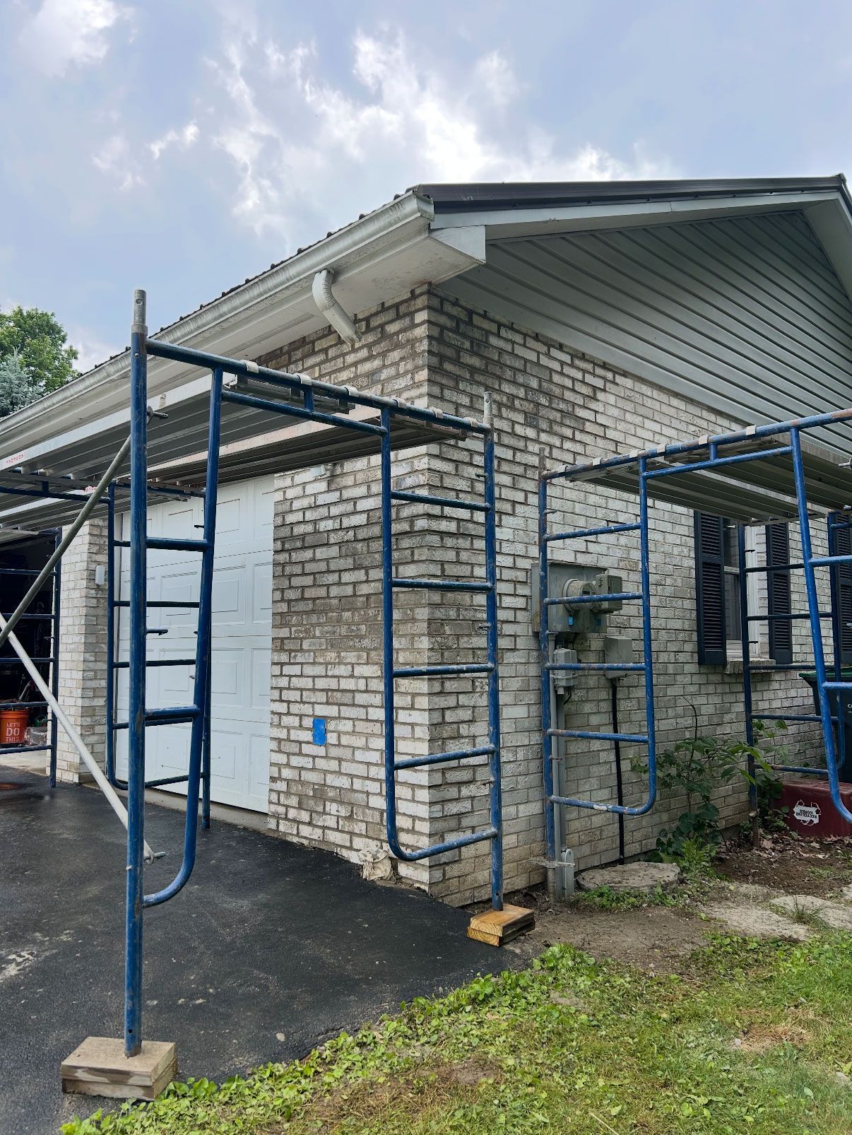 Brick house exterior with scaffolding, garage door, and siding under cloudy skies.