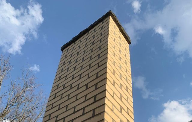 Tall brick chimney against a blue sky with clouds.