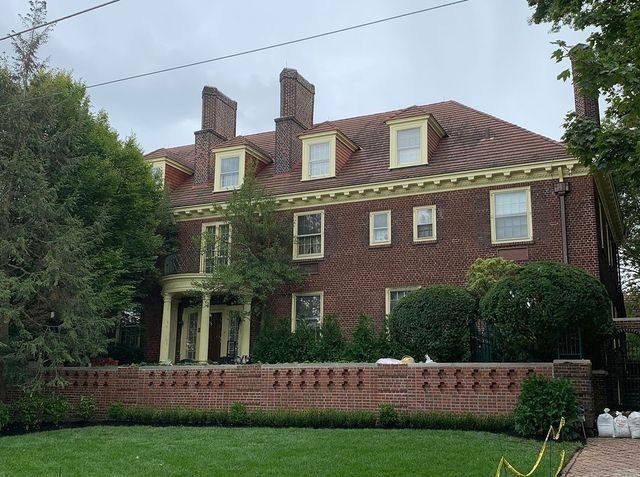 Brick mansion with red tile roof, dormers, and yellow trim. Features a low brick wall in front.