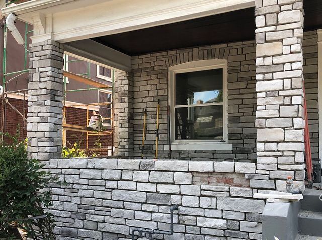 Stone facade being constructed on a porch with a window. Gray and white stone with scaffolding.