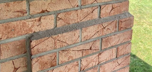 Close-up of a brick wall corner with a grey mortar and reddish-brown bricks, with a grassy background.