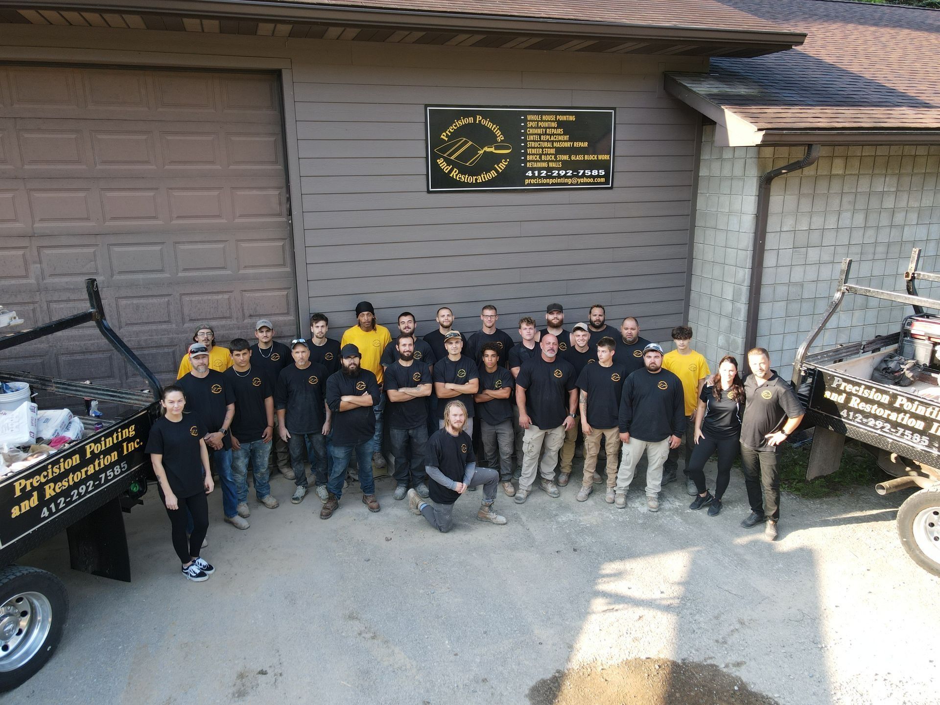 Group photo of a large team in front of a building with trucks, wearing black shirts and khakis.