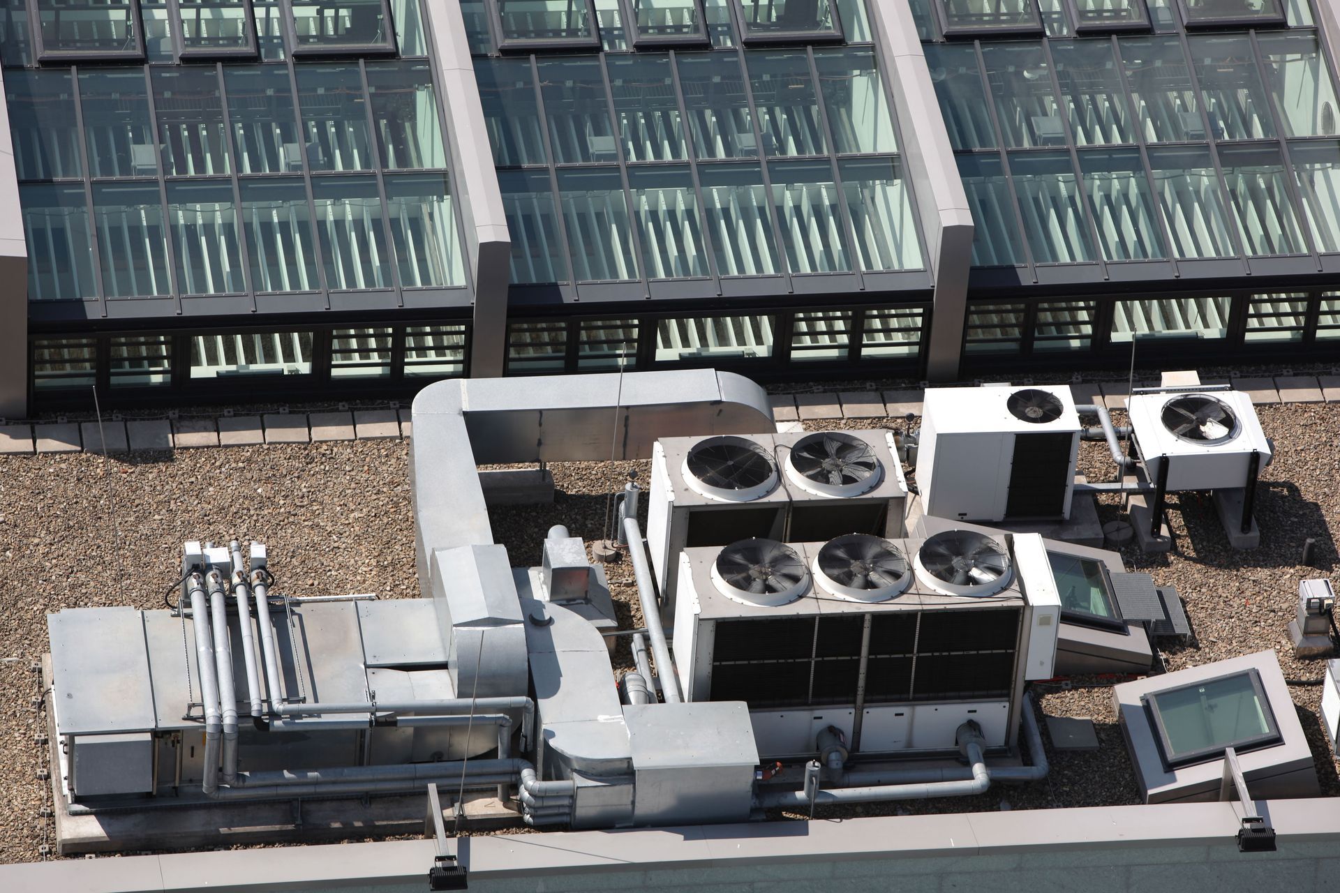 Rooftop HVAC units with fans and vents, set against a background of a glass-paneled building roof.