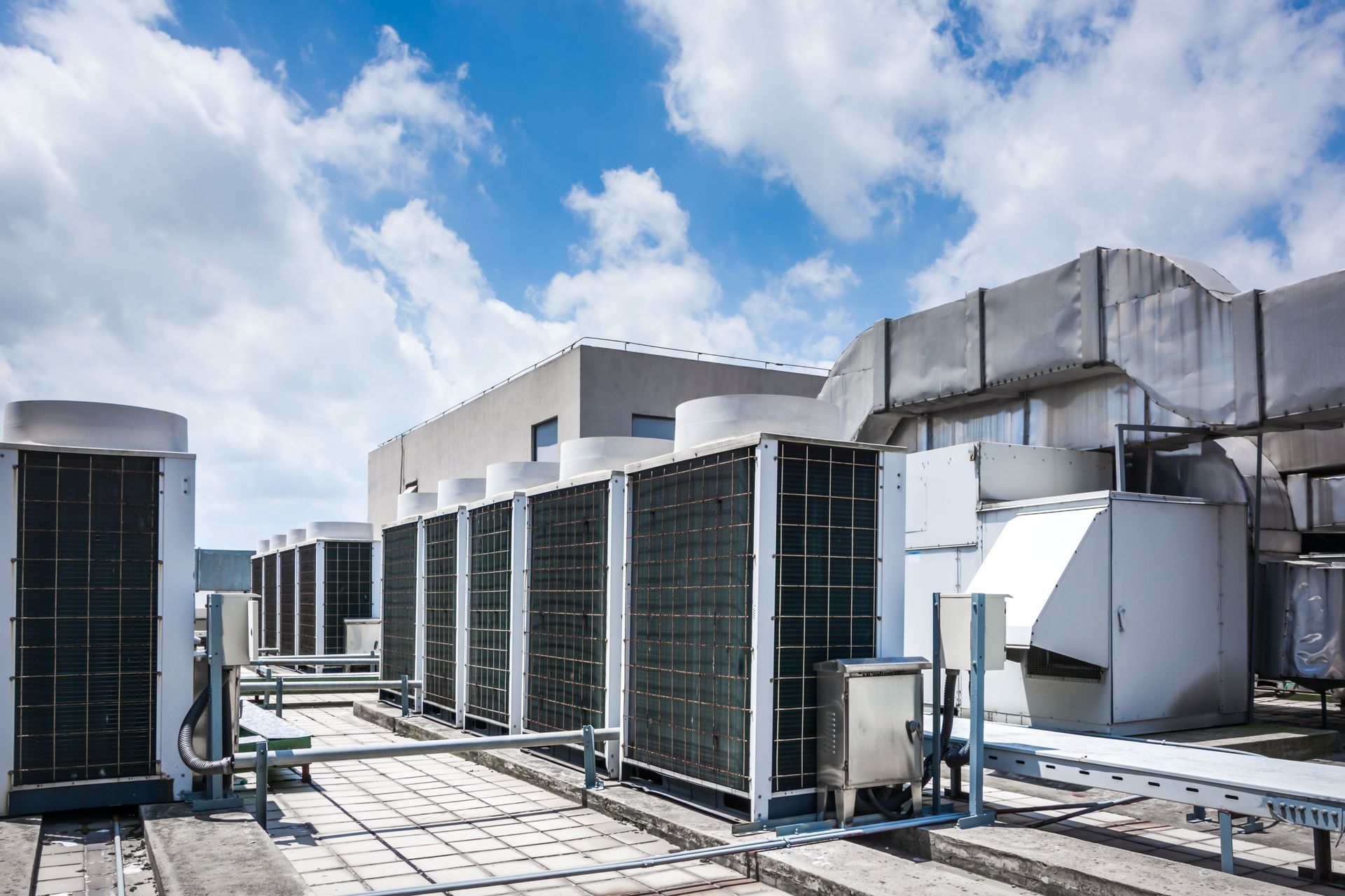 Rooftop air conditioning units on a building's roof with blue sky and clouds in the background.
