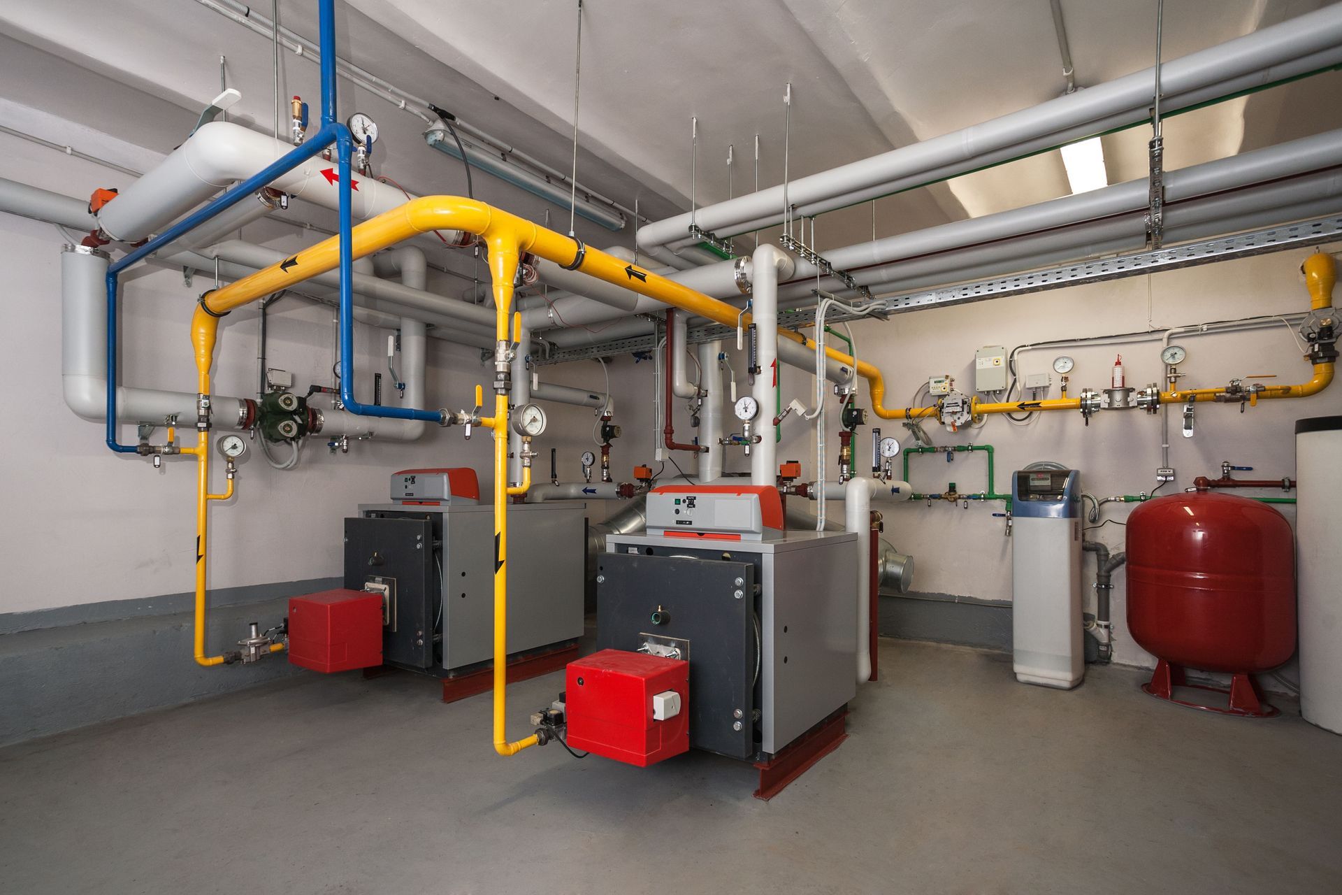 Heating system room with boilers, pipes, gauges, and water tank.
