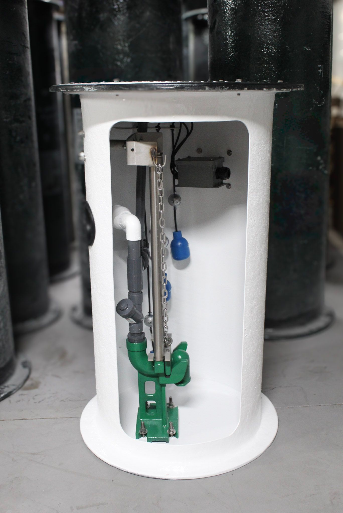A sump pump system in a white enclosure green pump, blue float, and gray chain visible.