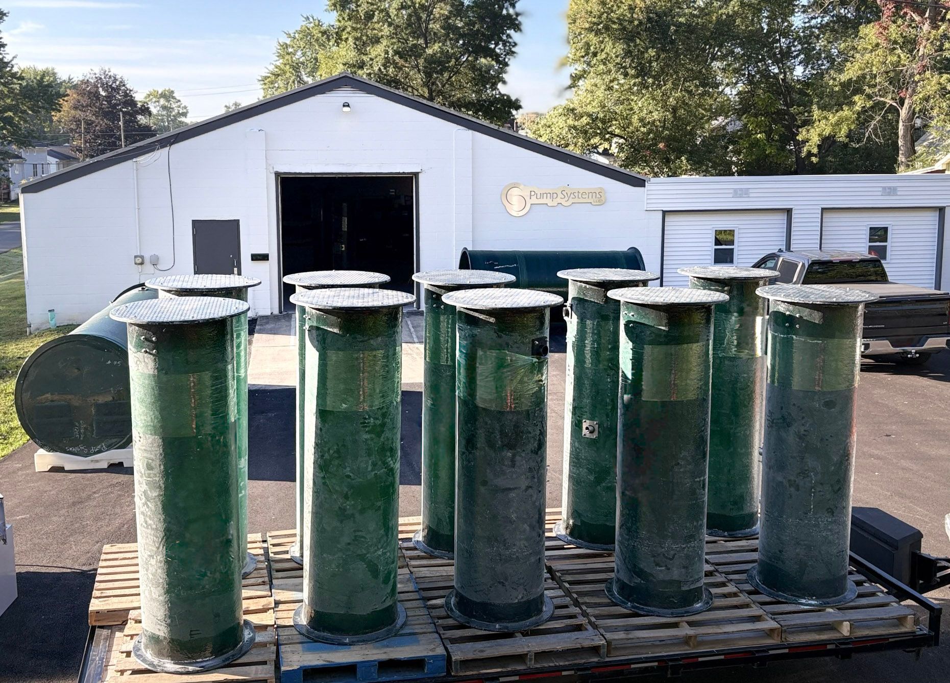 Green cylindrical containers on a pallet in front of a white building with open garage doors.