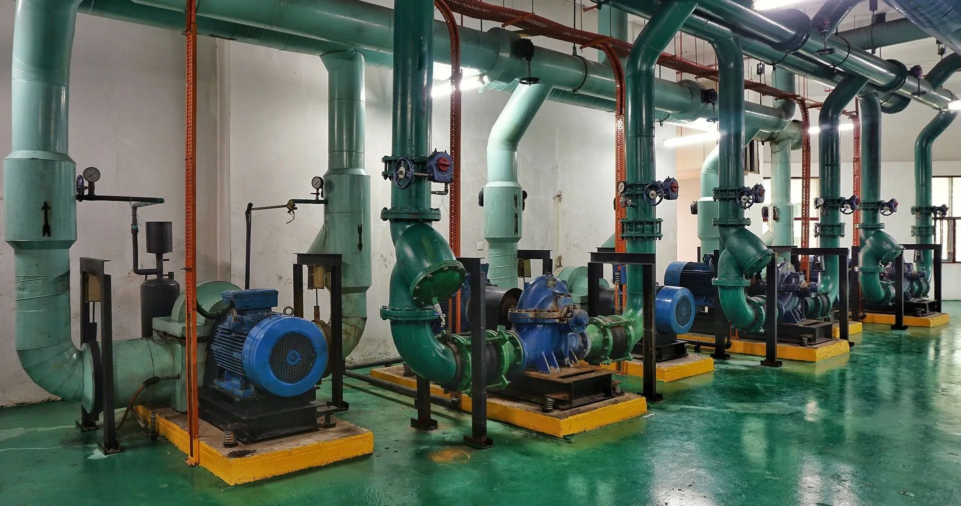 Industrial pumps, blue and green, with piping, in a utility room.