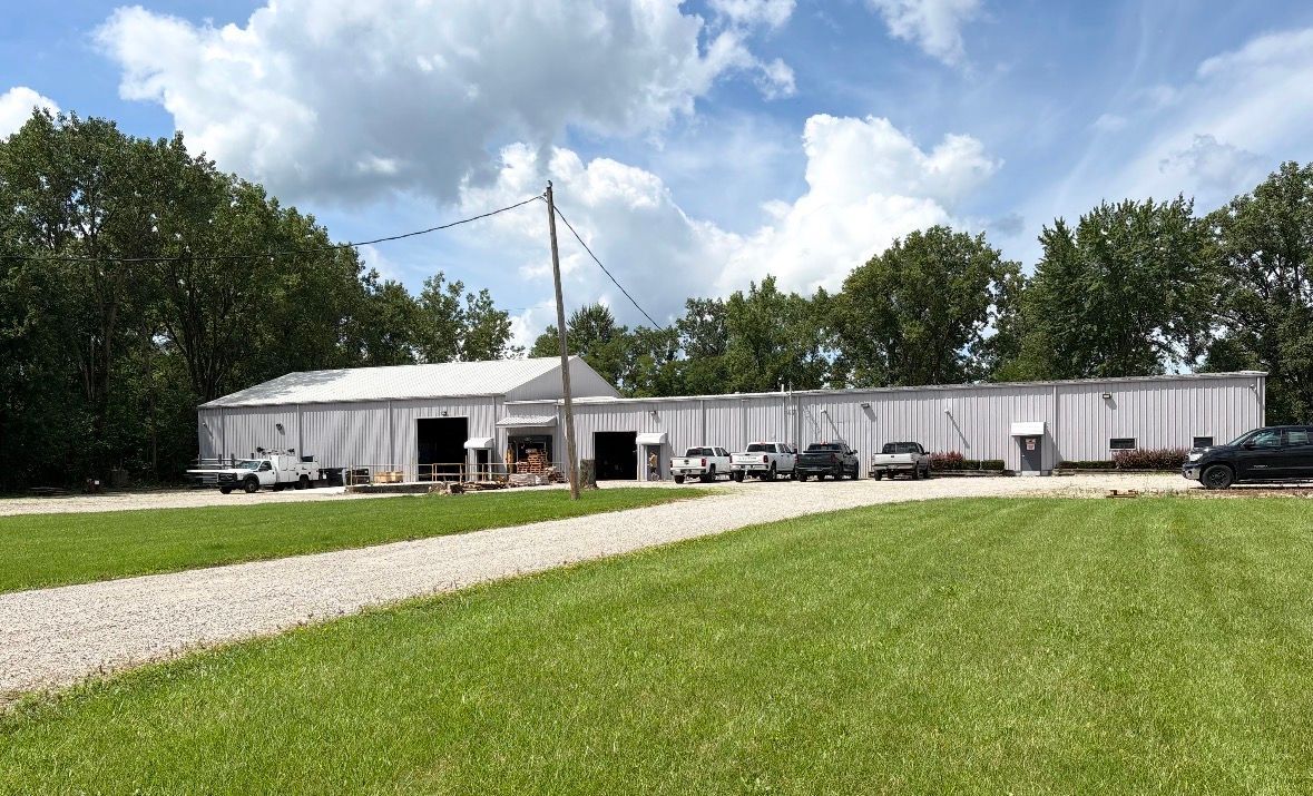 Long white building with a grassy foreground, trees, and a partly cloudy sky