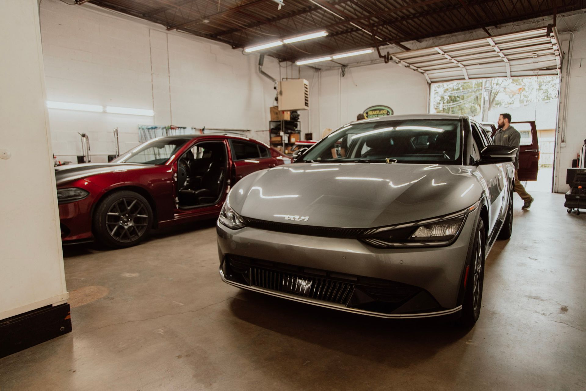 A gray Kia EV6 and a red car parked in a garage; a person stands near the doorway.