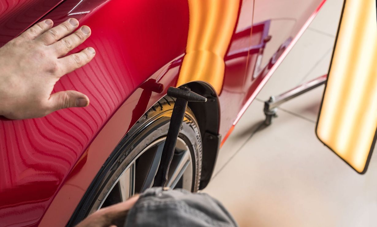 Hand touching a red car with dent repair tools and lighting.